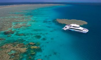 A large white boat anchored at a coral reef system with clear blue waters