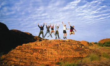 A group of backpackers on a rock in the Australian outback jumping and having fun during the 5 Day Outback Camping Adventure