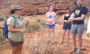 A group of backpackers and a local guide learning about local plants in the Australian outback during a 3 day Uluru adventure