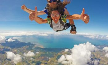 Two people skydving with the ocean and land beneath them