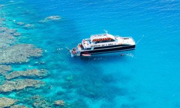 A three story dive boat anchored in the ocean beside a coral reef