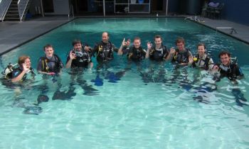 A group of friends in the swimming pool in scuba diving gear while training for their PADI open water course