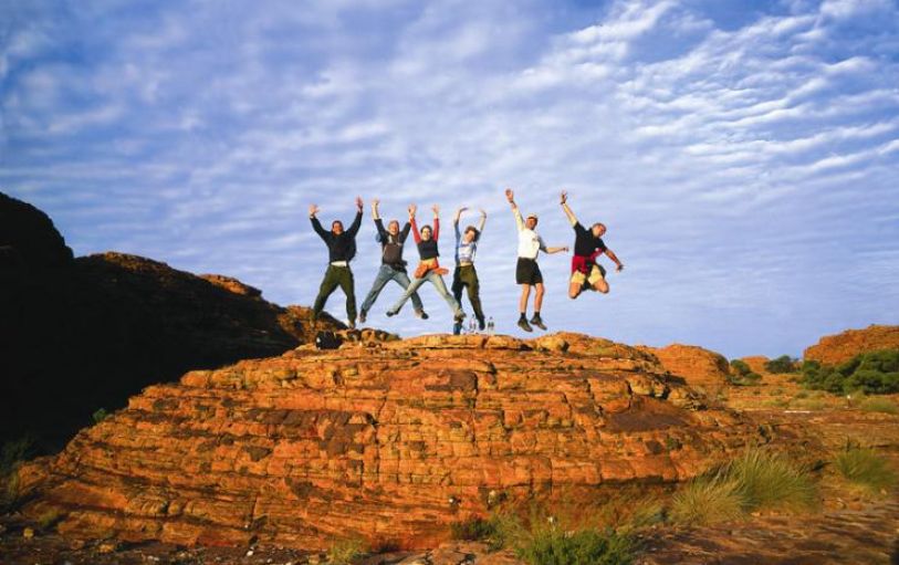 6 backpackers on top of a rock in the Austrlalian outback having fun and jumping in the air on the 3 night Rock the Center tour