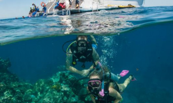 Two snorkellers on the Great Barrier Reef above a coral formation with a dive boat in the background