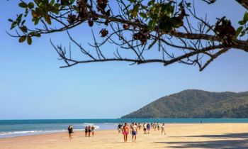 Long range shot of a group of friends walking along a secluded beach with the mountains in the background