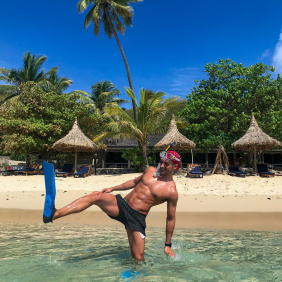 Image of man standing in crystal clear sea in Fiji with snorkel and flipper with the beach and palm trees in the background