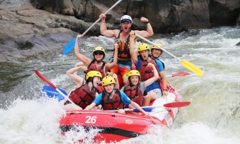A group of people in a raft travelling down river rapids wearing helmets and life jackets