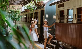 two girls in summer clothe boarding an old style train on a platform in a train station