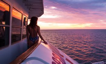A woman on the top deck of OceanQuest overnight dive boat watching sunset on the Great Barrier Reef