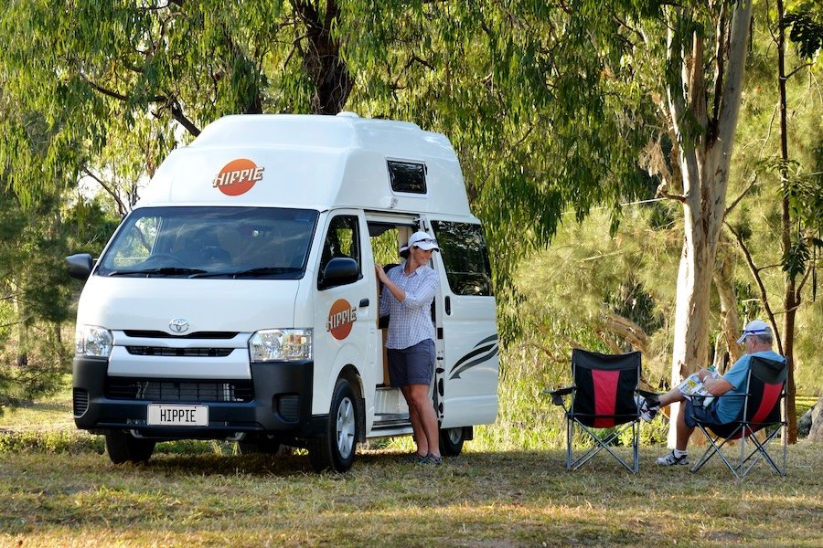 A couple in front of a hitop campervan rented from Peterpans