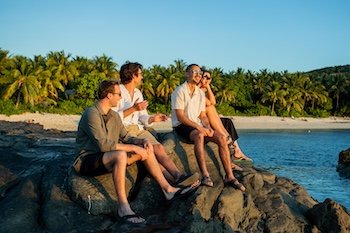 Four friends in Fiji relaxing on a rock and enjoying Sunset Barefoot Manta