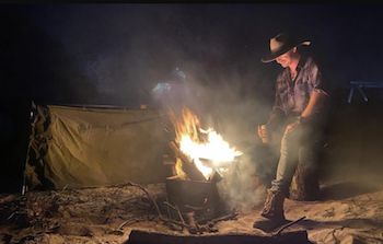 A man sitting beside a camp fire and a swag tent as part of the Kgari safari trip