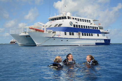 Three Scuba divers laughing and having fun in front of the Ocean Quest boat on the Great Barrier Reef