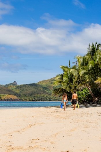 Two backpakcers walking with snorkelling gear on the beach in Fiji