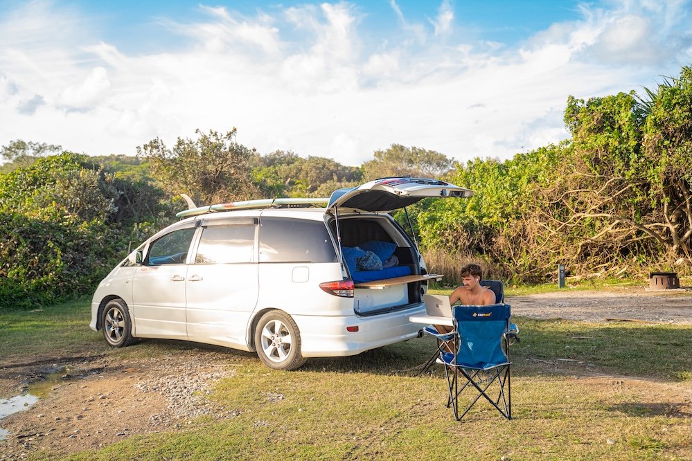 A backpacker sitting on a laptop outside an open sleeper car rented by Peterpans