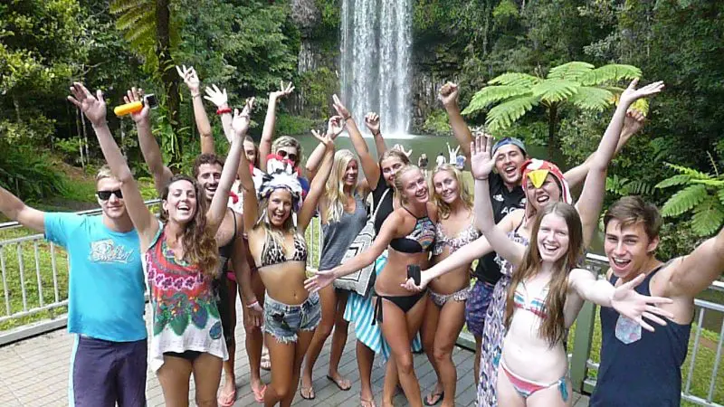 Joyful group in vibrant swimwear smiles by a stunning rainforest waterfall during a 1 Day Waterfall Wanderers tour adventure.