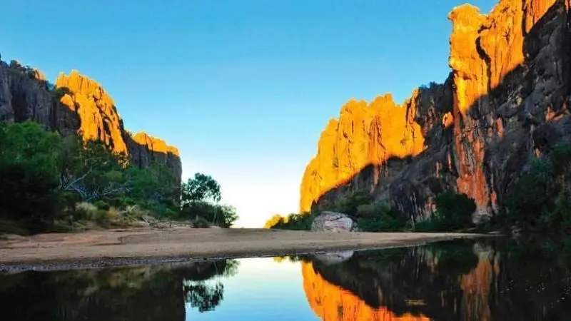 Sunlit cliffs mirrored in a tranquil river on the 10 Day Broome to Darwin 4WD Kimberley Adventure—breathtaking Australian outback scenery.