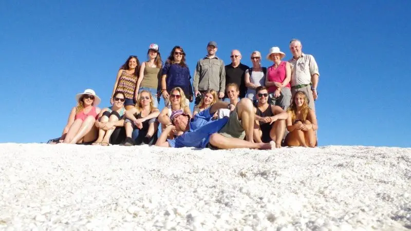Smiling travellers bask on pristine white sand beneath clear blue skies during the popular 6 Day Perth to Exmouth One Way Tour.