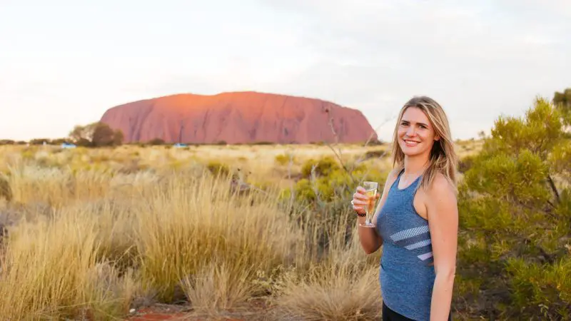 A woman drinks at sunset with Uluru in the background on the 3 Day Uluru Rock The Centre Tour from Alice Springs, Australia.