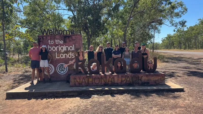 Travellers gather beside a Kakadu National Park sign, prepared for their 4-day Kakadu, Katherine & Litchfield adventure tour.