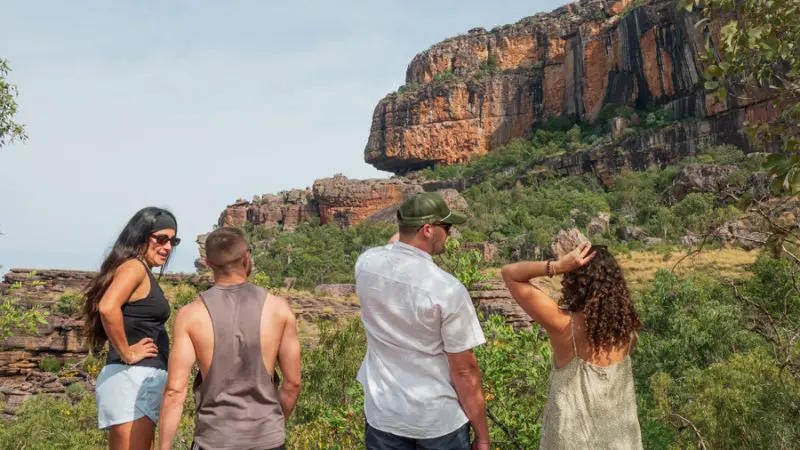 Four adventurers take in breathtaking Kakadu scenery on a 3-day camping tour, overlooking rugged cliffs and lush green wilderness.