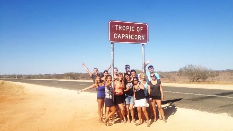 Travellers pose happily beneath the iconic Tropic of Capricorn sign on the sunny 6 Day Perth to Exmouth Tour in Western Australia.