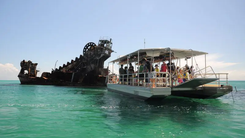 Experience the ultimate Moreton Island Day Pass as a group explores iconic rusted shipwrecks in crystal-clear turquoise waters under sunny skies.