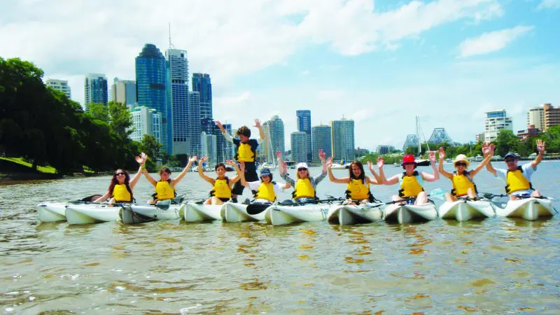 Group on a 1.5-hour kayak hire paddles in yellow life jackets, with vibrant city skyline views in the background.