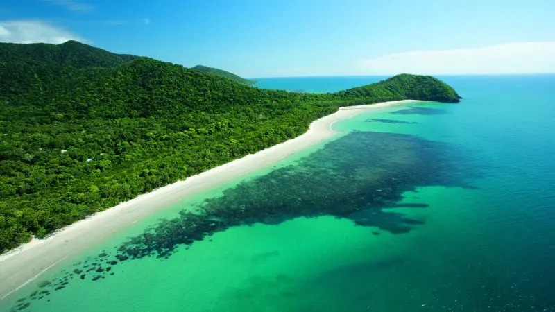 Aerial view of Daintree Rainforest beach with crystal-clear turquoise waters, pristine white sand, and vibrant green tropical hills.