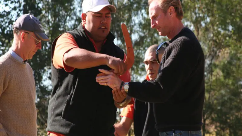 Group of four men on an Uncharted Blue Mountains Tour, enjoying a sunny day outdoors as one expertly demonstrates boomerang throwing skills.