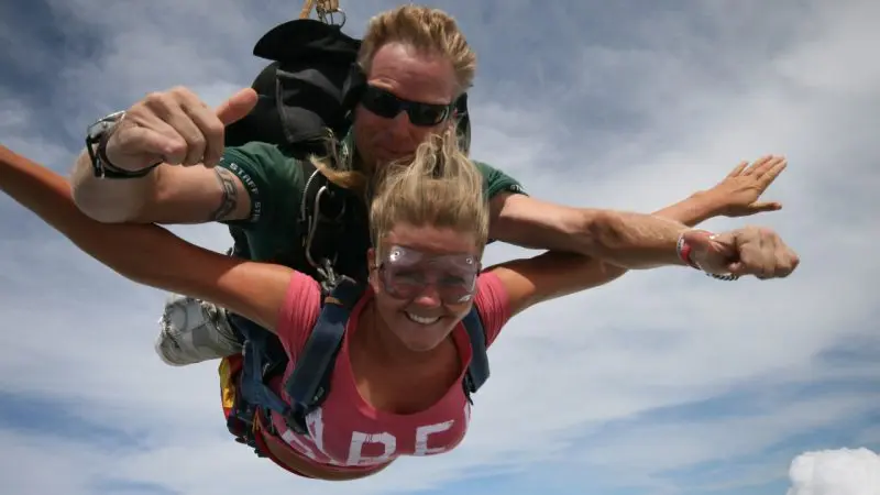 Two people tandem skydiving over Sydney, smiling and giving thumbs up above the clouds—experience top-rated Skydive Extras.