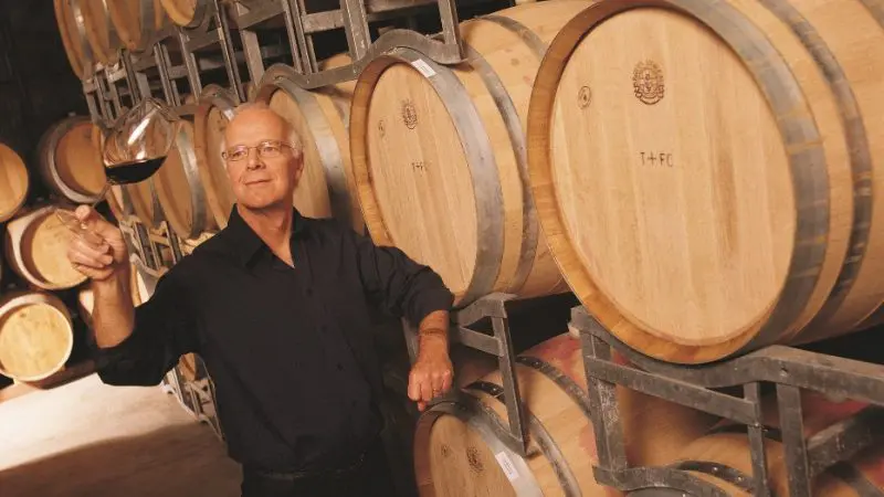 Yarra Valley Grazing Tour: man in atmospheric wine cellar showcasing premium red wine beside oak casks, highlighting local winery experience.
