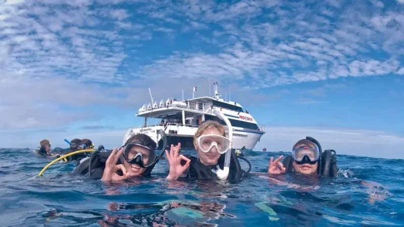 Three scuba divers signal OK underwater near a dive boat during a PADI Rescue Diver Course, demonstrating safe scuba diving skills.
