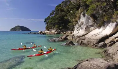 Four adventurers kayaking in crystal-clear turquoise waters near rocky coastlines and a distant island on the Three Day Classic tour.