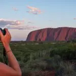 Two women photograph iconic Uluru on a 3-night Rock The Centre Yulara adventure, with dramatic clouds enhancing the Outback landscape.