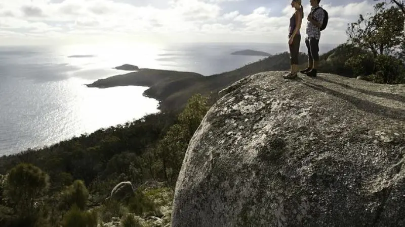 Two travellers on a rocky outcrop admire stunning Wilsons Promontory coastline during a top-rated 1 Day Go West Tours adventure.