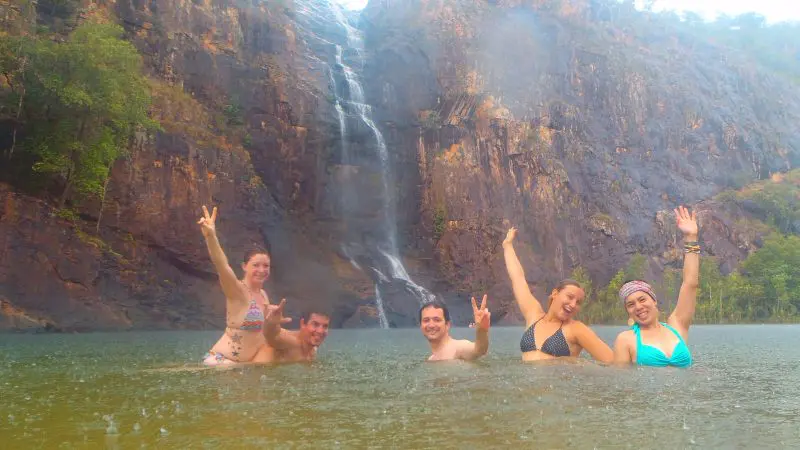 Group of five in colourful swimsuits stands beside a breathtaking Kakadu waterfall, showcasing top attractions on guided Kakadu tours.