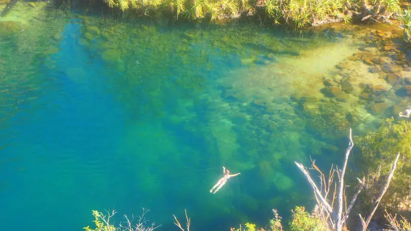 Person relaxing on their back in a crystal-clear blue pool on a Kakadu Koolpin Tour, lush greenery and scenic rocks all around.