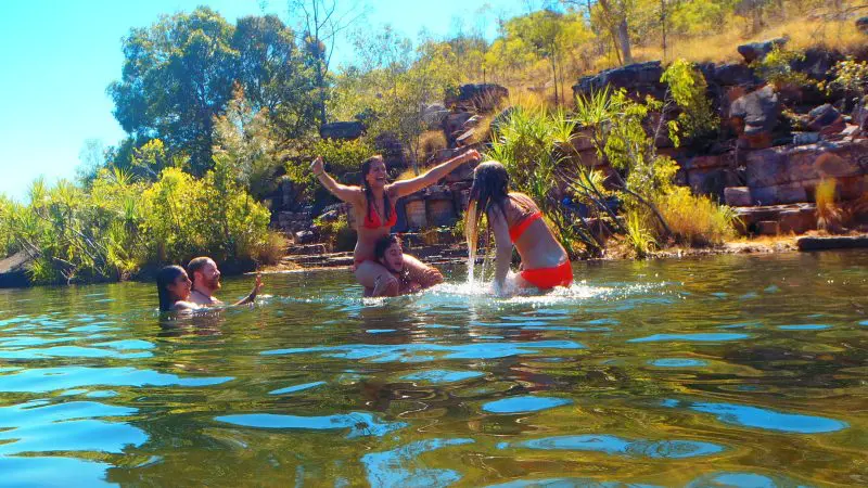 Group of four enjoying an idyllic Kakadu swimming hole, surrounded by lush greenery and rocks under the bright Australian sun.