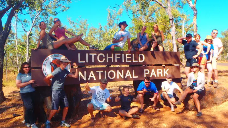 Travellers gather beside a prominent Litchfield National Park sign under clear skies during a 3 Day 4WD Kakadu Litchfield tour.