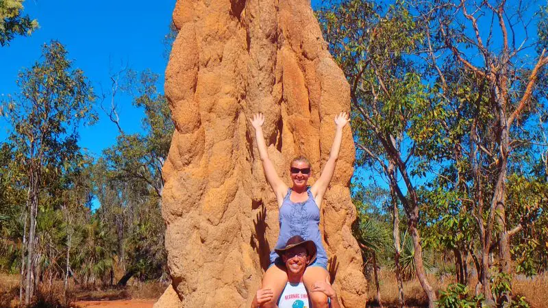 Two adventurers stand beside a towering termite mound amid lush trees on a 3 Day Kakadu Litchfield 4WD tour in Australia.