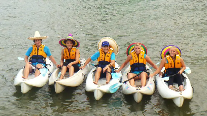Group of five wearing life jackets and sombreros kayak together happily, paddling on the water during a 1.5-hour hire session.