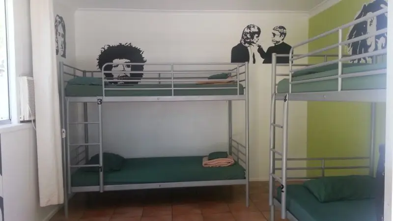 Spacious, sunlit dormitory room featuring sturdy metal bunk beds with fresh green bedding, ideal for your 3 Day Kgari Adventure in Rainbow Beach.
