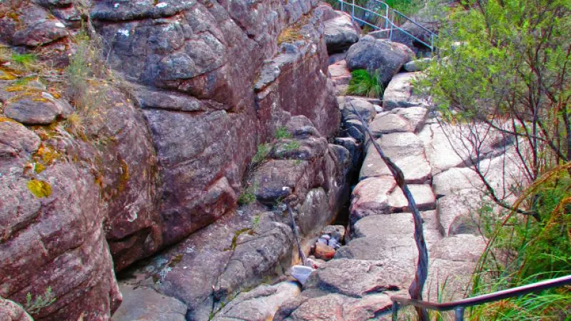 Scenic Grampians Day Tour: narrow rocky trail with railings winding through dramatic gorge, flanked by towering steep rock walls.