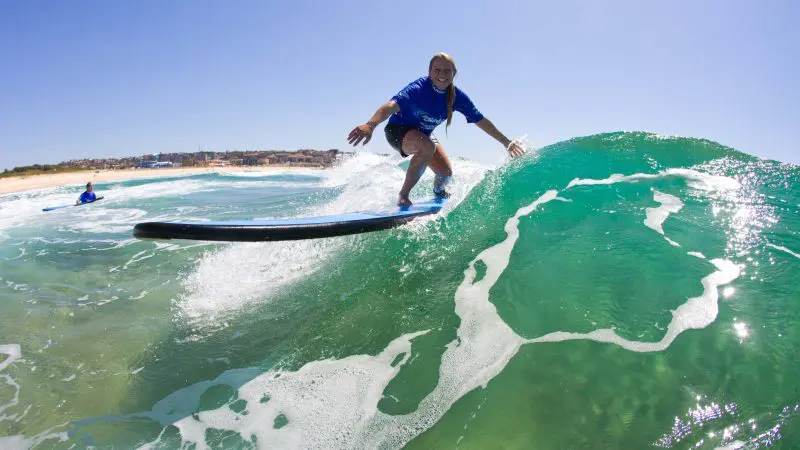 Experience the thrill of surfing a vibrant green wave near Byron Bay’s sandy beach on a sunny day—Half Day Surf Tour adventure.