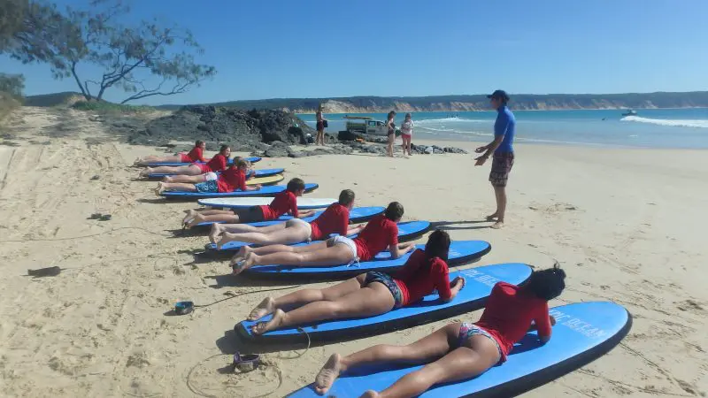 Surf instructor teaches group in red shirts to catch waves on Australia’s longest wave beach during an exciting beach drive adventure.