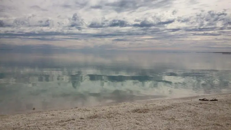 Serene cloudy sky reflected on tranquil ocean, sandy beach, and flip-flops—ideal scene for a Perth to Exmouth 6 Day One Way Tour.