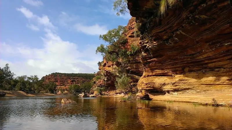 Scenic river winds past striking layered red rock cliffs, a must-see attraction on the 6 Day Perth to Exmouth One Way Tour.