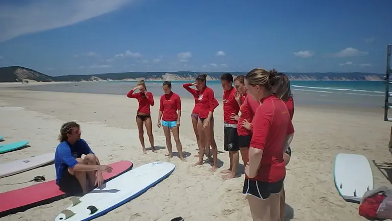 Surf instructor guides red-shirted students mastering surfing techniques on Australia’s renowned longest wave beach for beginners.