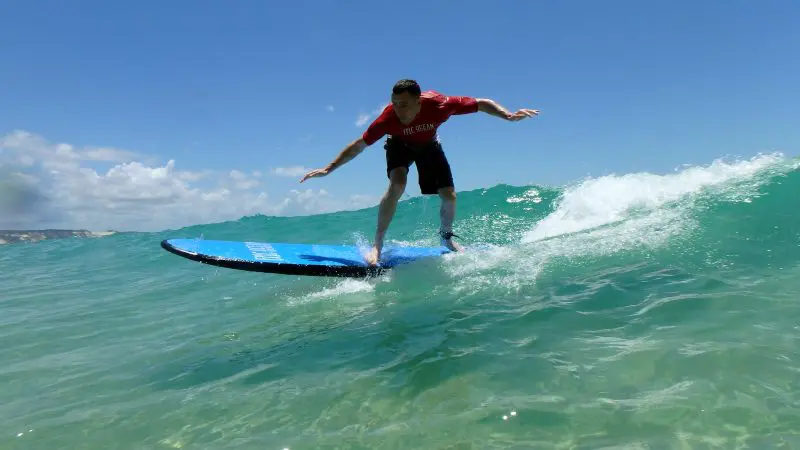 Surfer riding Australia’s longest wave on a blue surfboard, after a picturesque Beach Drive, beneath a vivid clear blue sky.